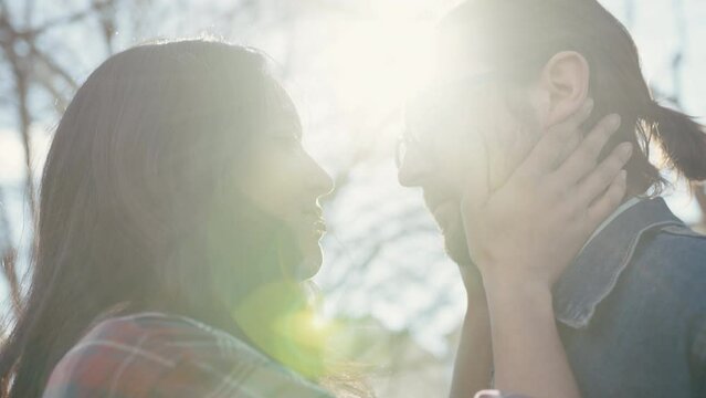 A couple kiss while woman holds man face outside with sun flare