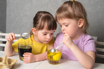 Children color eggs with food coloring. Sisters painting Easter eggs.