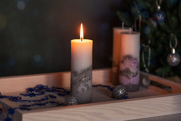 Festive background with decorative candles and lights. Burning candle and Christmas decoration on a wooden tray, close-up, front view, low key, selective focus.