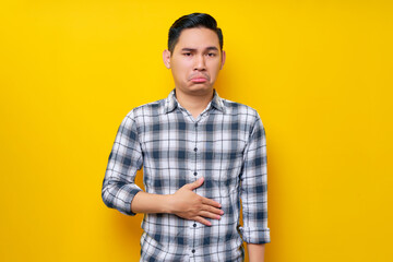 Young handsome Asian man wearing casual clothes keeps his hands on his stomach feeling hungry and...