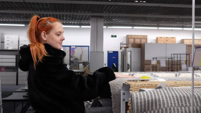 A young girl chooses carpeting in a store. The girl checks the softness of the carpet to the touch. Sale of carpets, paths, interior and decor items.