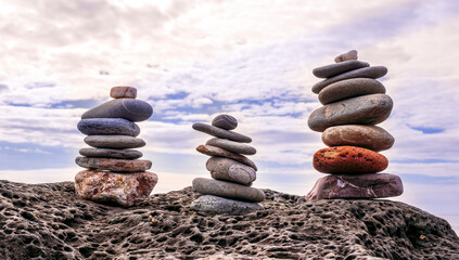 small turrets on a sea coast, flat stones stacked in little towers on ocean beach with water and blue sky background , immersive travel concept landscape