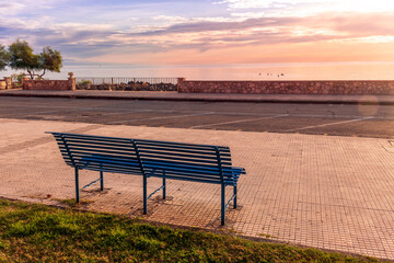 Naklejka na ściany i meble metallic bench on sea embarkment with asphalt road and beautiful seashore landscape with amazing cloudy sky