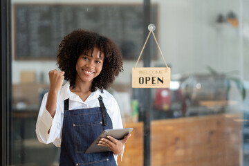 Happy young African American small business owner feeloing excited about the sales of the coffee shop, looking into digital tablet.