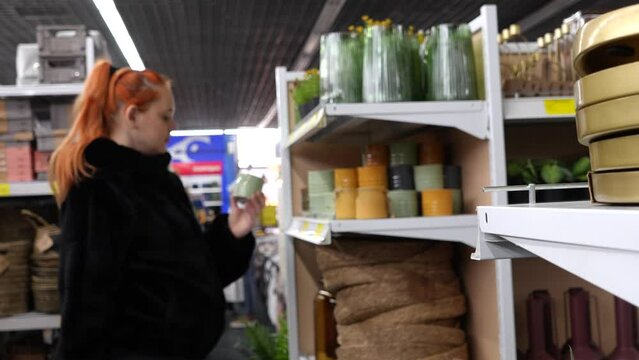 Shelves in a store with interior and home decor items. In the background, out of focus, a girl is examining a small ceramic vase.