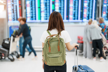 Young woman with backpack looking at the flight time information board in international airport,...