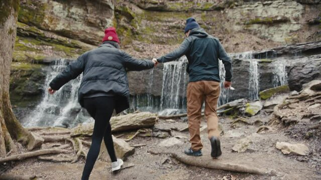 Man and woman walk on rocks next to water fall and sit down