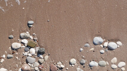 Fototapeta na wymiar The wave crashes on the seashore. Sea and beach background. Sandy beach, water and sea foam. Seashore, pebbles and sand. Texture of the sea, beach, pebbles