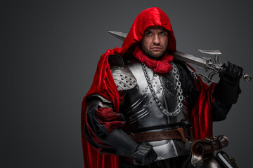 Shot of dark knight dressed in steel armor and red robe against gray background.