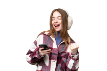 Young pretty woman wearing winter muffs over isolated chroma key background with phone in victory position