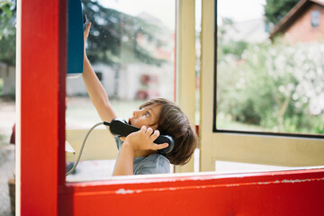Curious boy reaching at telephone buttons in booth