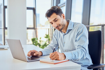 Businessman taking down notes in diary by laptop at office