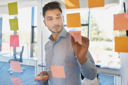 Businessman sticking adhesive notes on wall in office