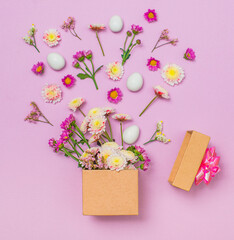 Spring flowers and easter eggs floating from gift box over violet background.