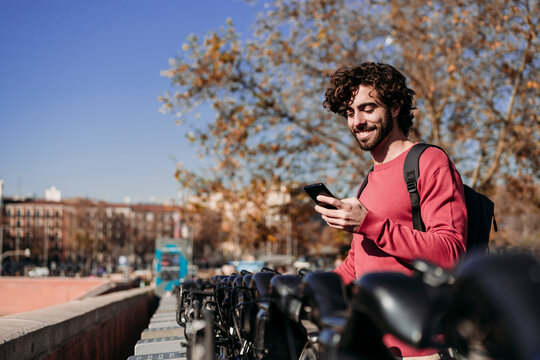 Happy man using mobile app to rent electric push scooter on sunny day