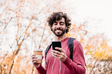 Happy man using mobile phone and holding coffee cup standing at footpath