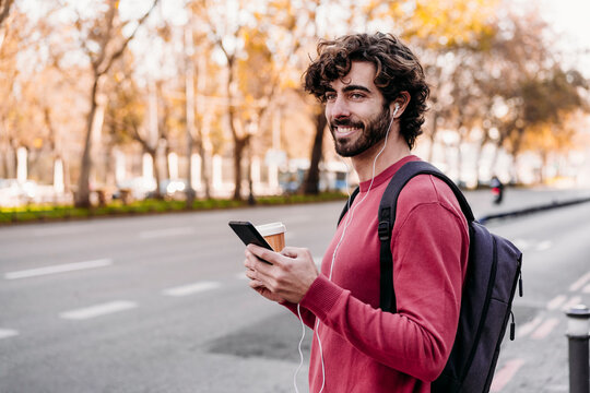 Smiling man with smart phone standing at sidewalk