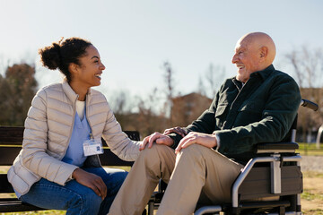 Happy caretaker with senior man sitting on wheelchair in park