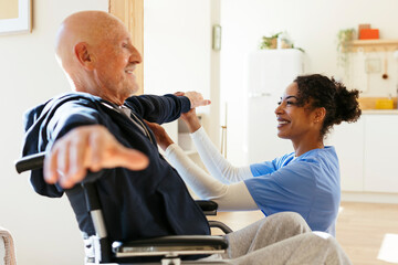 Smiling physical therapist examining senior man stretching arms at home