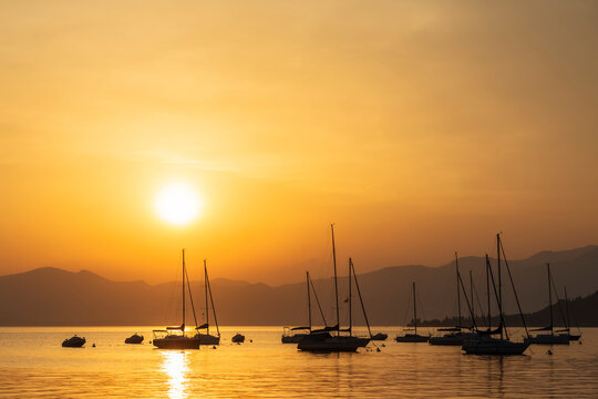 Italy, Veneto, Bardolino, Silhouettes of sailboats floating in Lake Garda at sunset