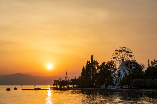 Italy, Veneto, Bardolino, Lake Garda at sunset with Ferris wheel in background