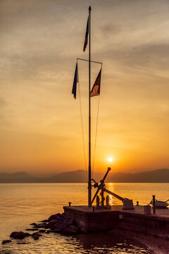 Italy, Veneto, Bardolino, Harbor flagpole at sunset