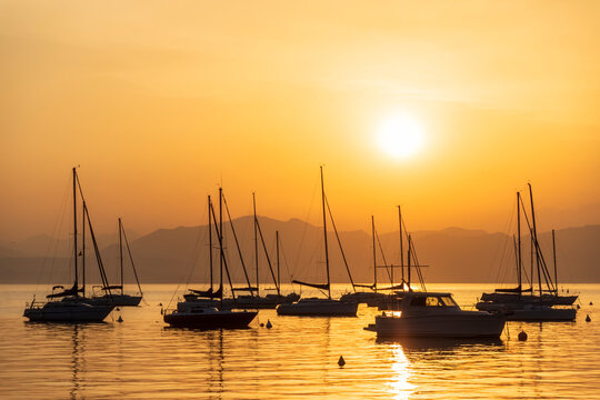 Italy, Veneto, Bardolino, Silhouettes of sailboats floating in Lake Garda at sunset