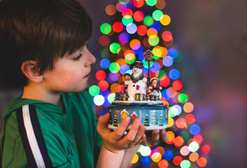 Boy holding Christmas decoration with tree lights in background.