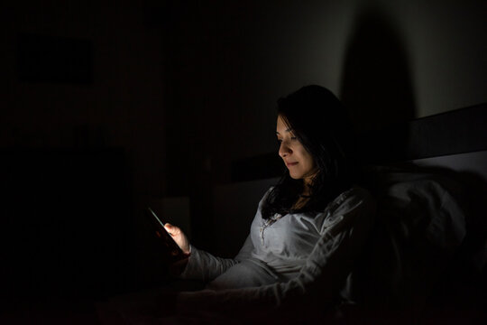 Latino woman using her cell phone before bed