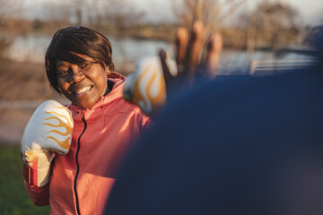 Senior woman wearing boxing gloves punching man at sunset