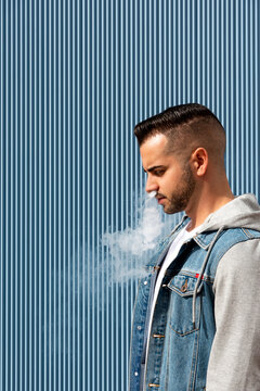 Young man smoking with an electronic cigarette over blue background