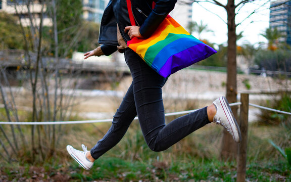 Lesbian woman jumping with a pride and reusable bag.
