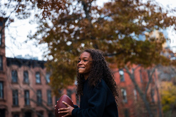 Smiling girl looking away while practicing American football in city
