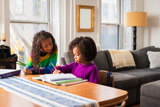 Girl assisting sister in doing homework at table in living room