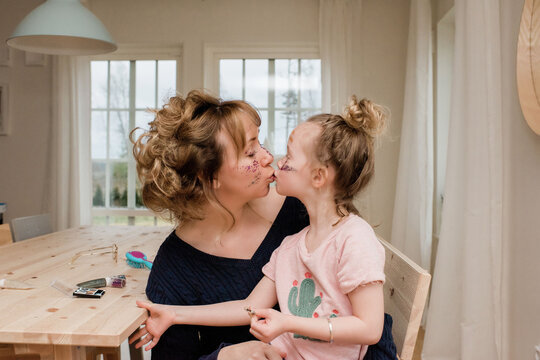 mother kissing daughter whilst they play with make up at home