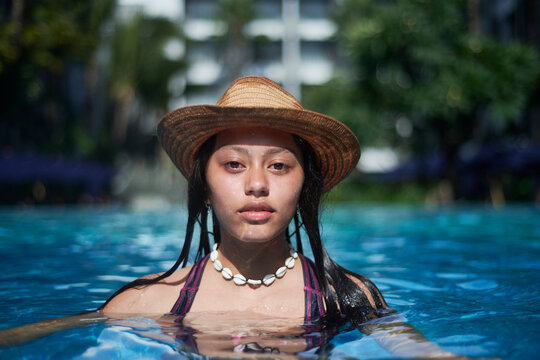Stylish trendy young teen visco girl in the pool wearing a straw hat