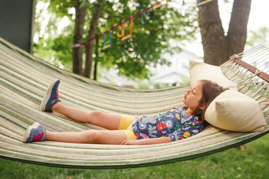 A little girl lays on a hammock by self in sunshine with closed eyes