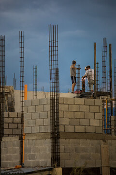 Two construction workers work or rooftop, welding metal railing.