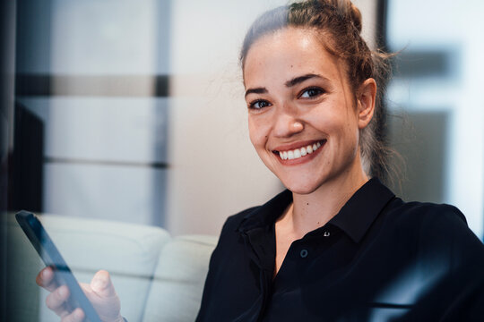 Happy young businesswoman with smart phone seen through glass