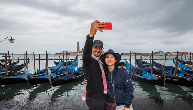 Thai couple taking selfie in front of parked gondola's in Venice