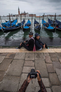 woman taking picture of couple with gondola's in Venice