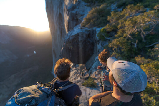 Three hikers looking at The Nose El Capitan from the top at sunset
