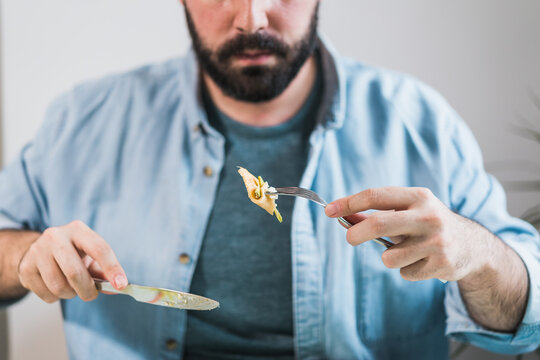 A plate of pancakes with cheese and avocado is on the table. An anonymous man is eating