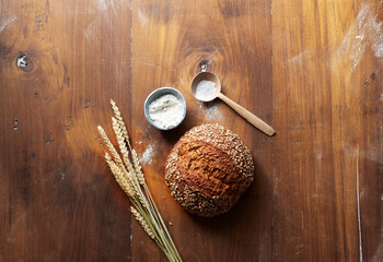 Wheat, flour and freshly baked loaf of bread on wooden table