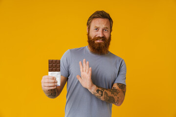 Bearded man doing stop gesture while holding chocolate bar