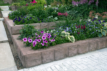 Flowerbeds in the garden with a stone fence. Perennial and annual flowers, landscaping, gardening, hobbies.