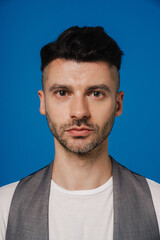 Young man looking at camera while standing isolated over blue wall