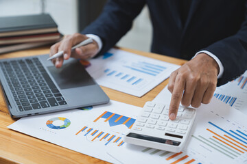 Asian businessman working in the office, calculating financial reports, organizing paperwork using a laptop and calculator as an aid.management concept accounting.