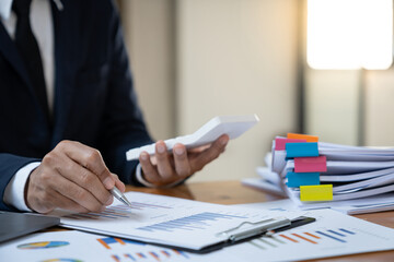 Asian businessman working in the office, calculating financial reports, organizing paperwork using a laptop and calculator as an aid.management concept accounting.