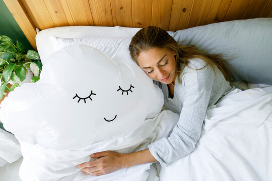 Woman hugging cloud balloon in bed at home
